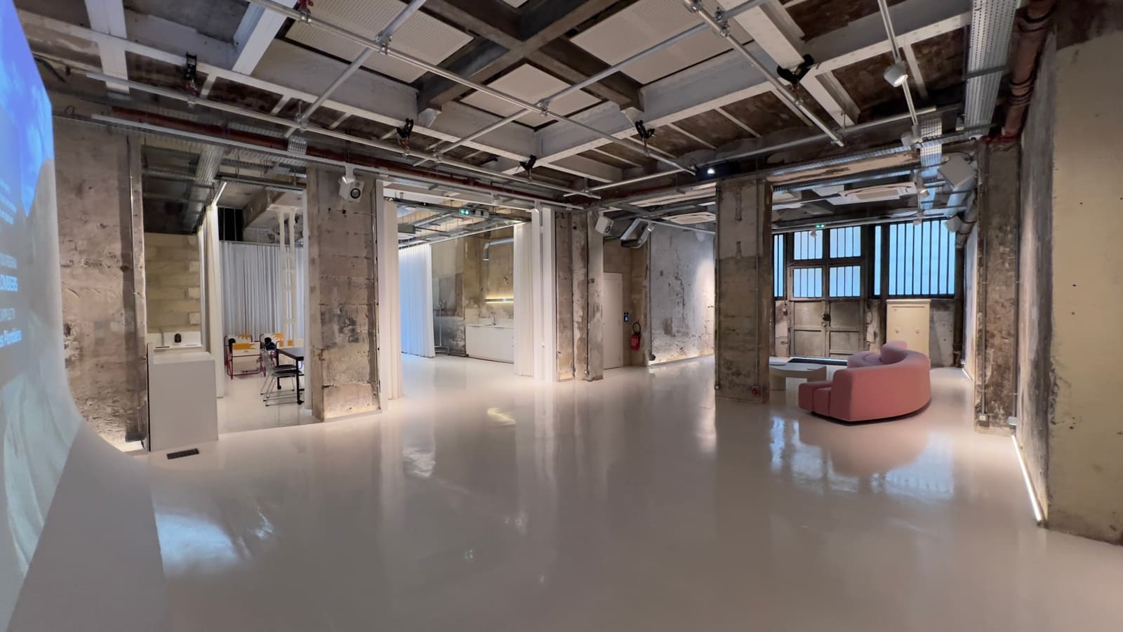 La grande salle de L'Atelier, vide — sol clair, poteaux bruts, verrière au fond